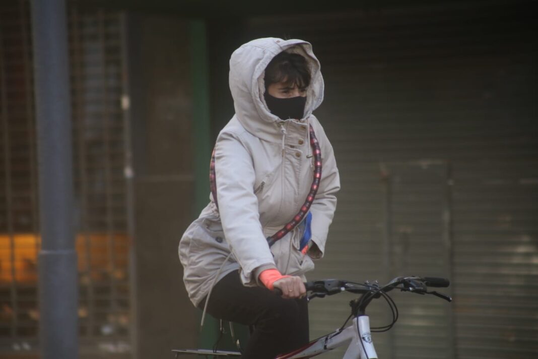 Mujer en bicicleta con abrigo grueso y capucha durante mañana fría en La Plata por ola polar.