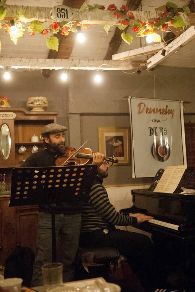 Cristian Luzza tocando el violín en la casa de té de Dennehy, con otro músico al piano de fondo